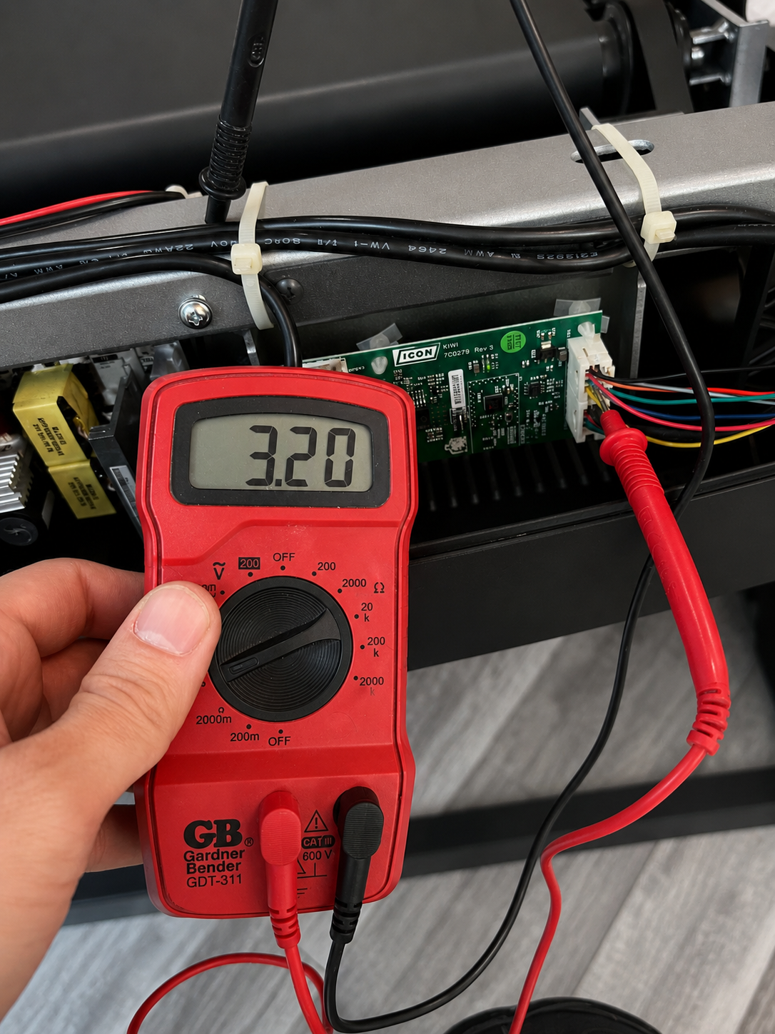 Multimeter testing treadmill electronics during diagnostics.